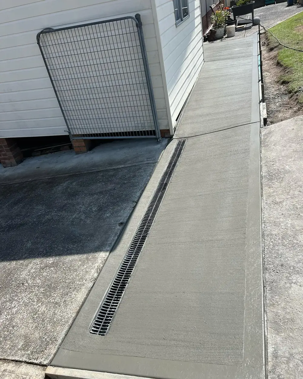 Narrow concrete pathway beside a house with drainage channel